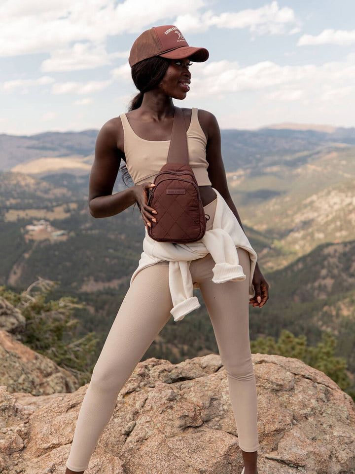 Person wearing a brown quilted sling bag standing on a mountain with a scenic background