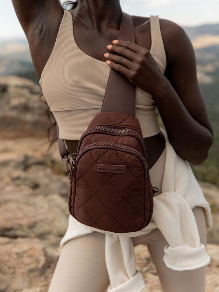 Person wearing a brown quilted crossbody bag in a natural setting