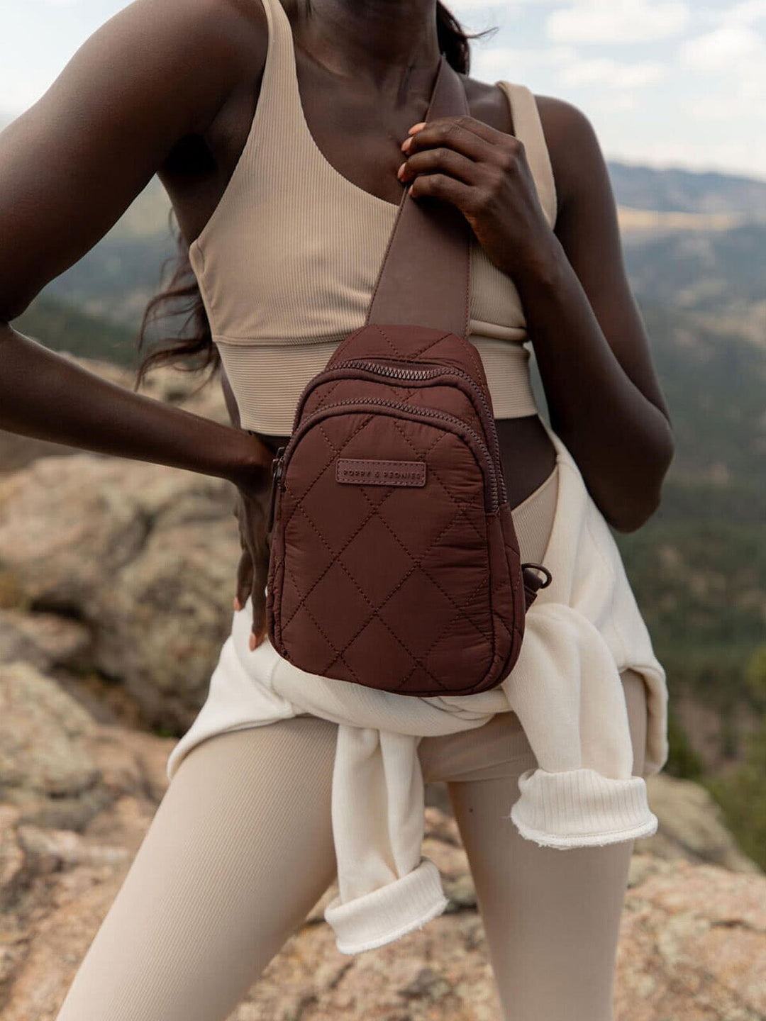 Person wearing a brown quilted sling bag with a scenic mountain background