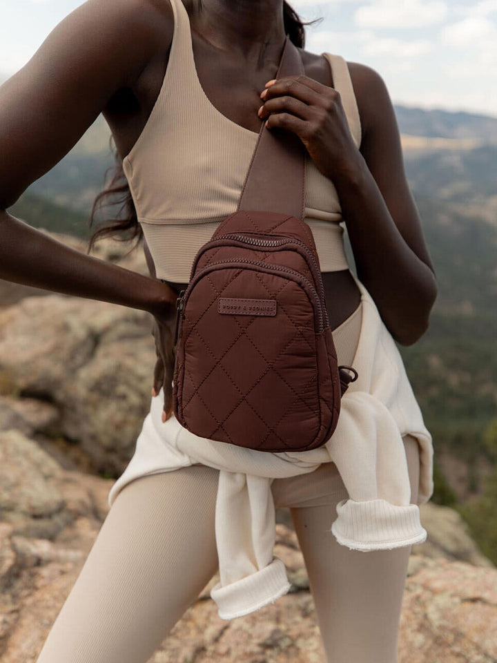 Person wearing a brown quilted sling bag with a scenic mountain background