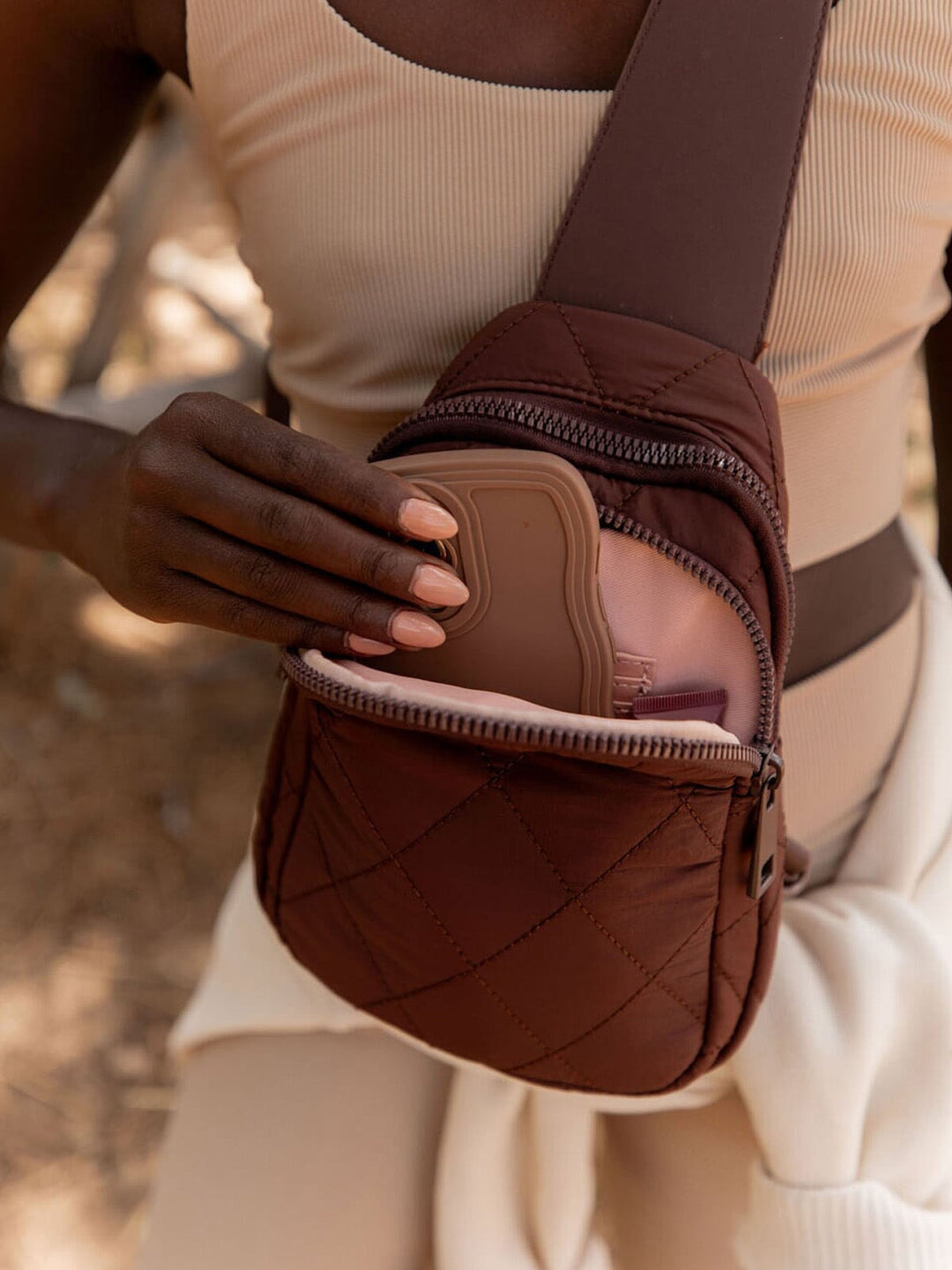 Person pulling a phone of our a brown quilted bag 