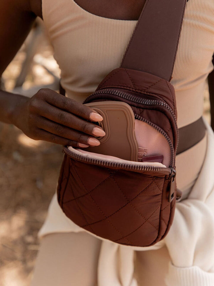 Person pulling a phone of our a brown quilted bag 