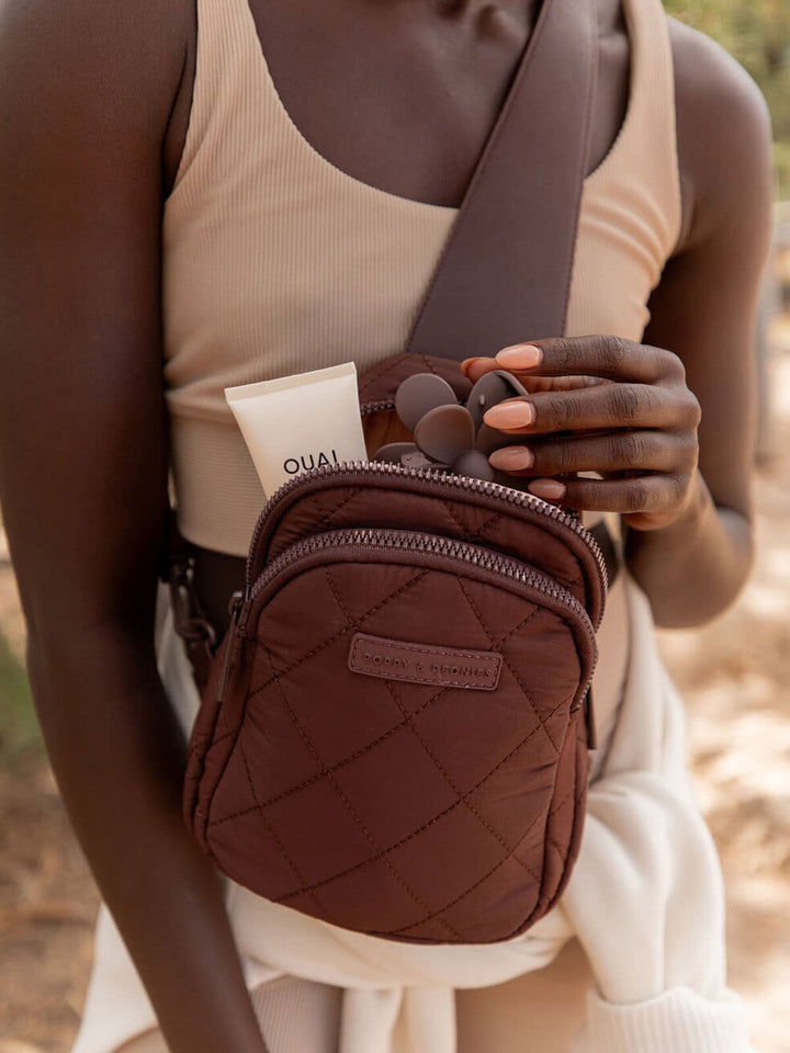 Person holding a brown quilted bag with a visible brand logo, wearing a beige top.