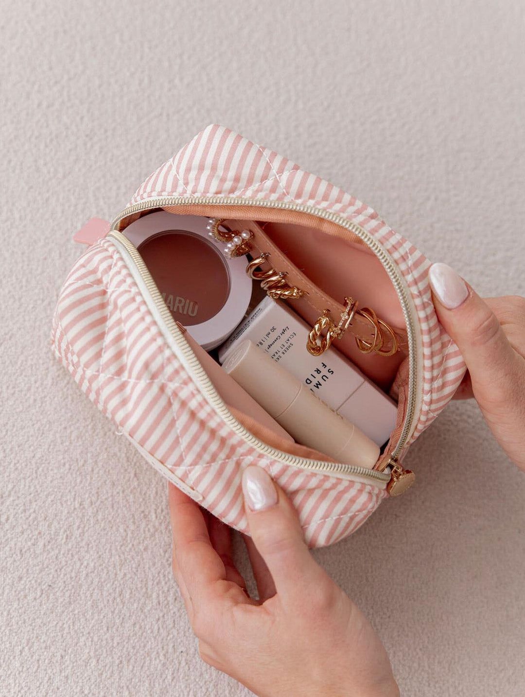 Small pink and white striped pouch held by a hand, containing cosmetic items.