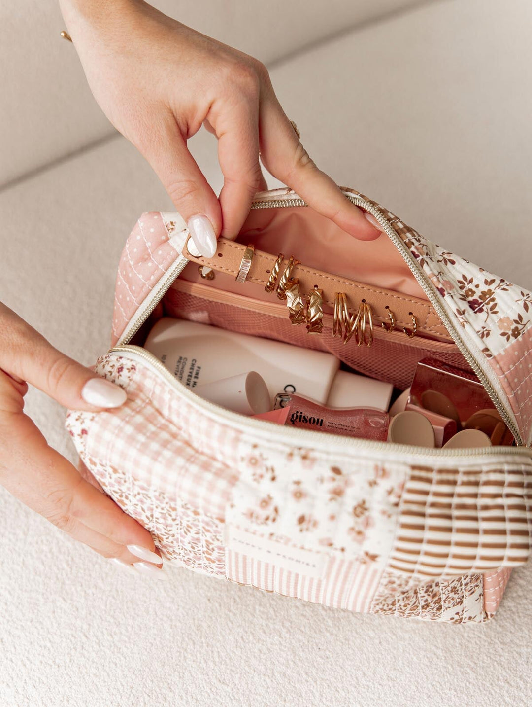 Pink patchwork makeup bag with skincare products and jewelry on a light background