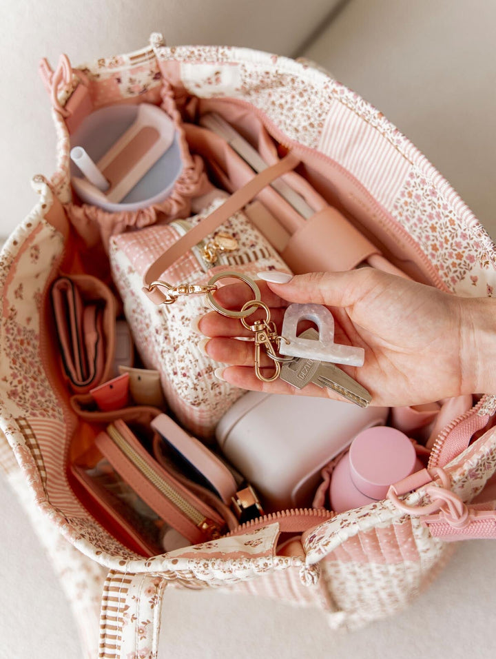 Hand holding keys over a pink and white handbag with various items inside
