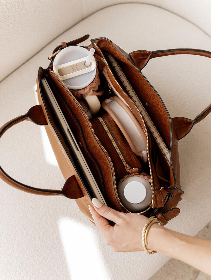 Open brown vegan leather tote bag with water bottles, headphones, and more inside.