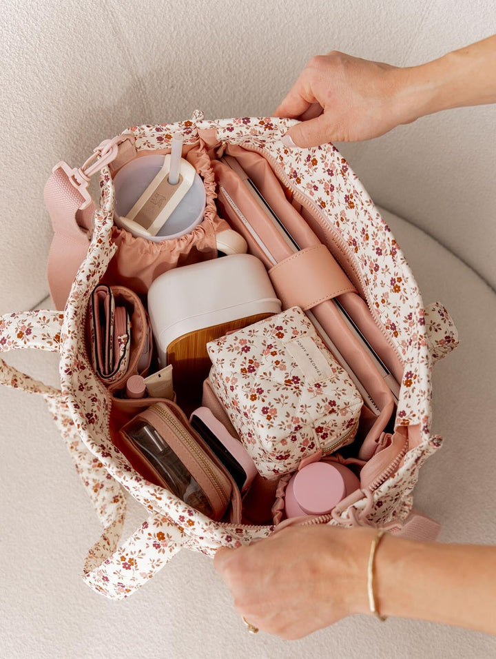 Floral-patterned tote bag filled with daily essentials held by a person.