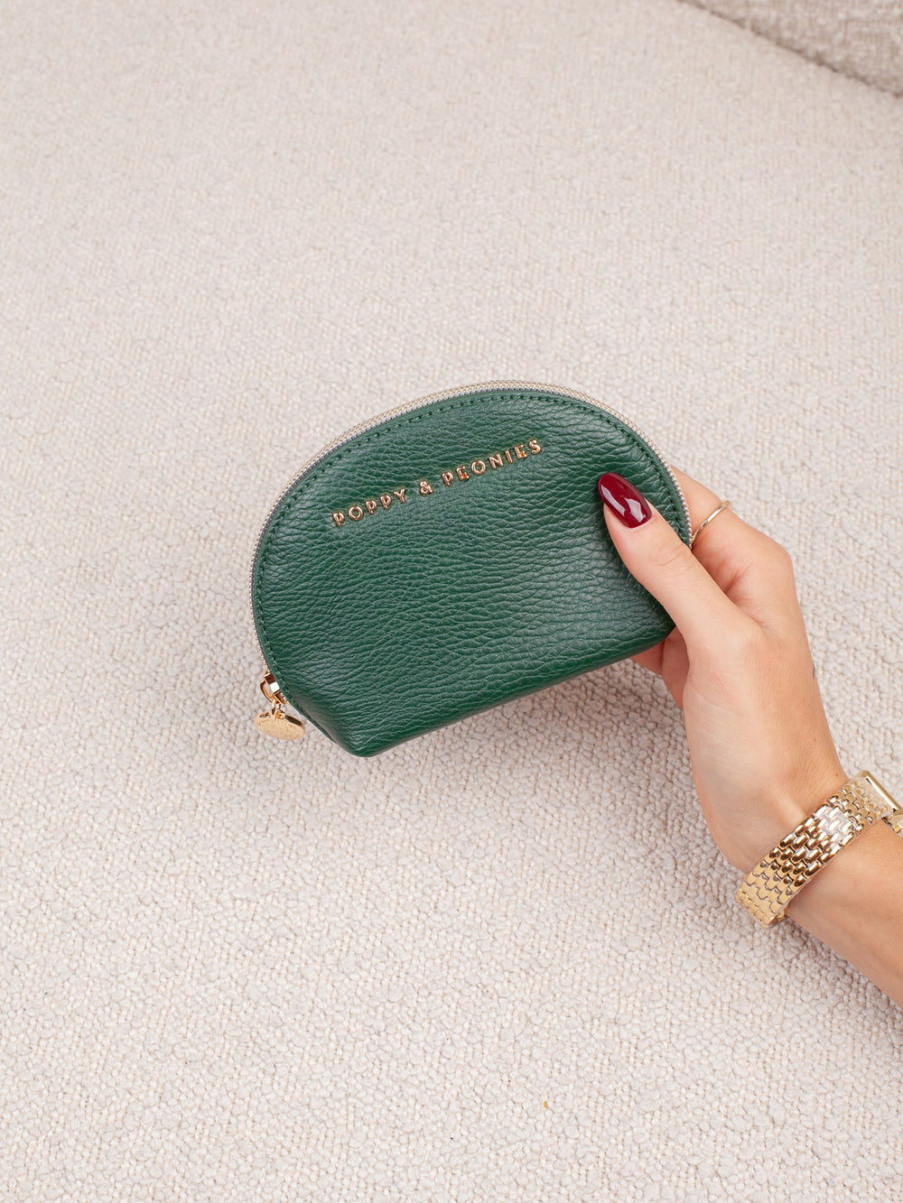 Product-focused lifestyle shot of the Knot Today Jewelry Case in Heritage Green, showcasing its compact rounded silhouette, textured exterior, and gold-tone branding.