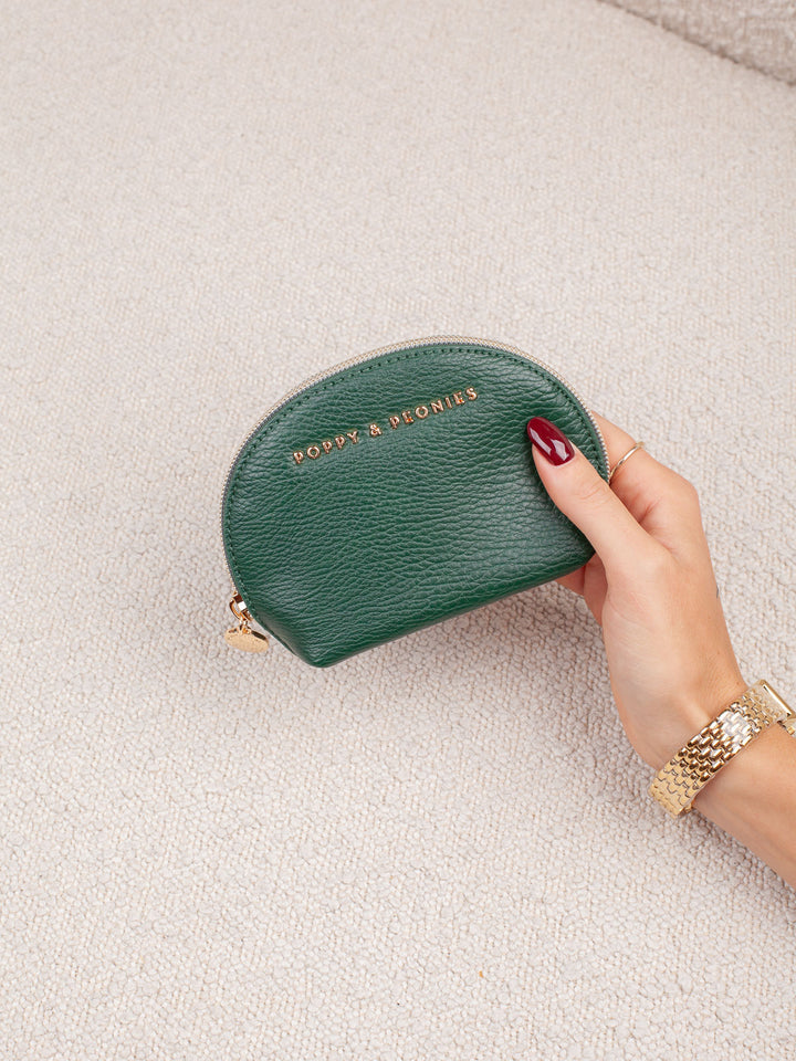 Product-focused lifestyle shot of the Knot Today Jewelry Case in Heritage Green, showcasing its compact rounded silhouette, textured exterior, and gold-tone branding.