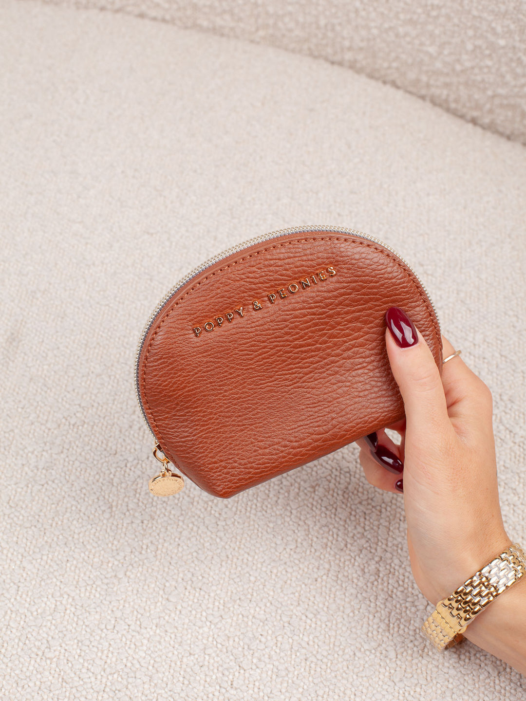 Product-focused lifestyle shot of the Knot Today Jewelry Case in Cognac, showcasing its compact rounded silhouette, textured exterior, and gold-tone branding.