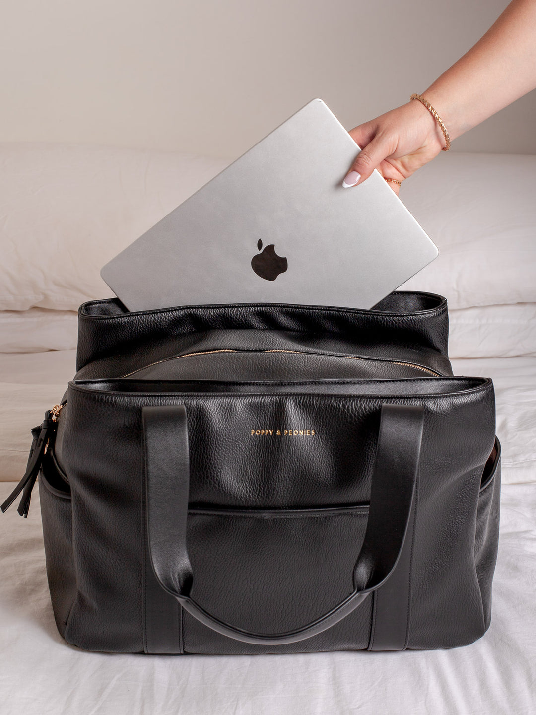 Lifestyle shot of the Poppy & Peonies Mini Voyager in Black, shown with a laptop being placed inside to highlight its spacious interior, laptop-friendly storage, black exterior, front pocket, and sturdy shoulder straps.