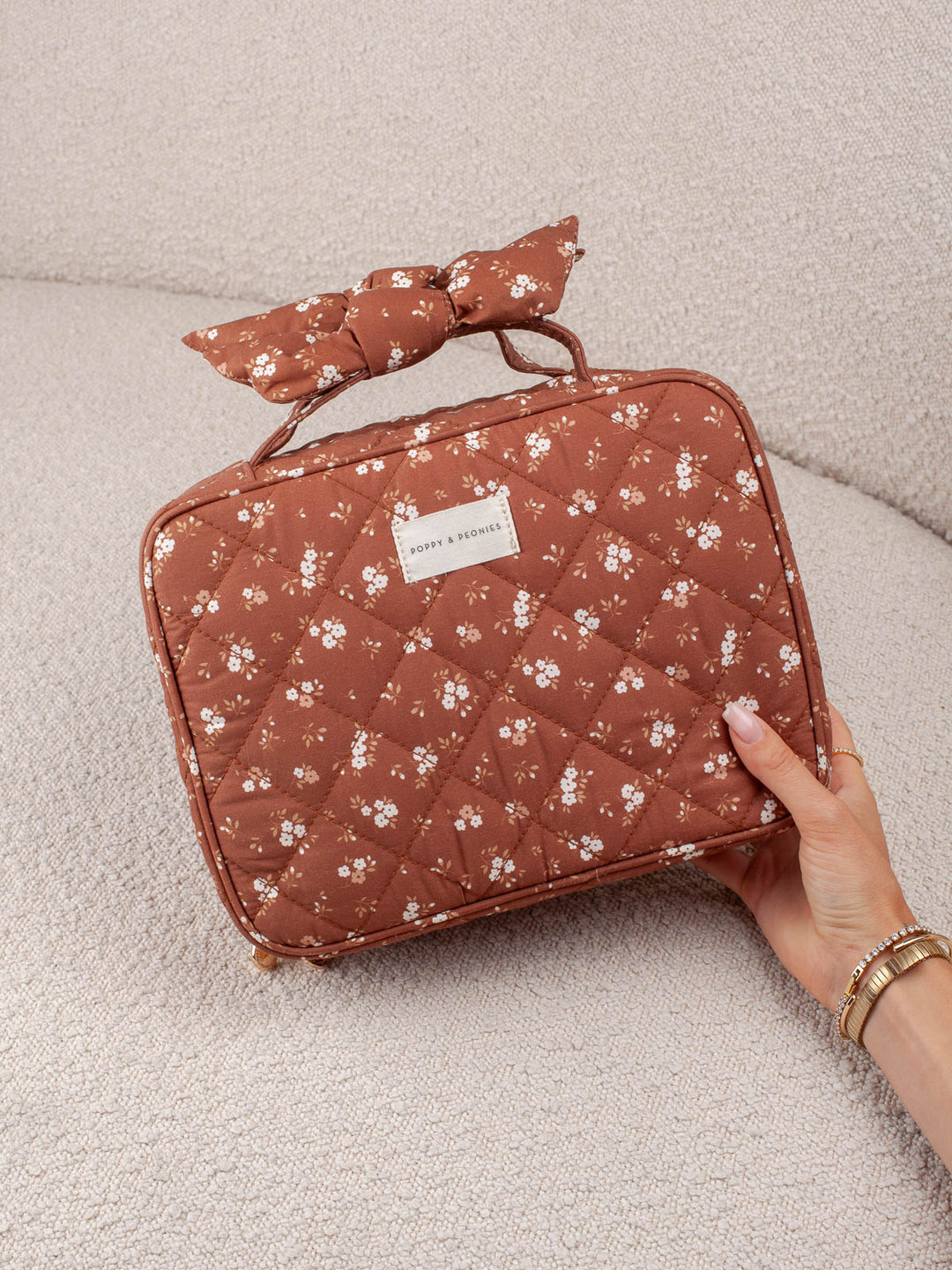 Product-focused lifestyle shot of the Small Hook Me Up in Brown Floral, highlighting its quilted floral exterior and coordinating bow handle.