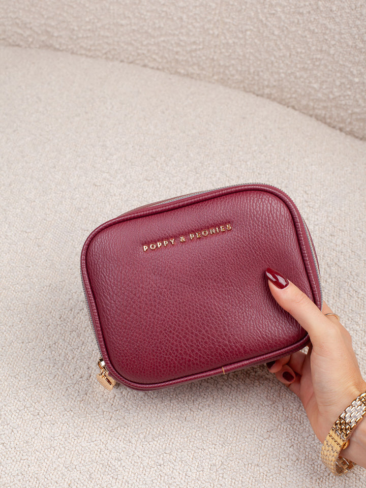 Handheld lifestyle shot of the Poppy & Peonies Pretty Connected Case in Berry, showcasing its rich berry exterior, structured silhouette, and gold-tone branding.