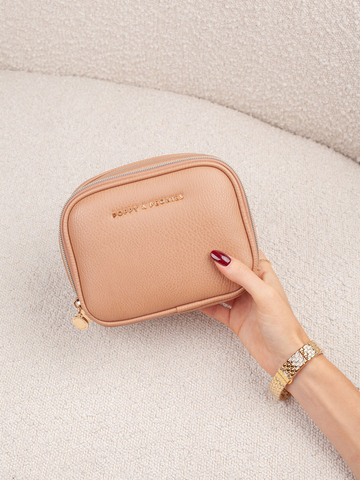 Handheld lifestyle shot of the Poppy & Peonies Pretty Connected Case in Taupe, showcasing its rich taupe exterior, compact structured silhouette, double-zip design, and gold-tone branding.