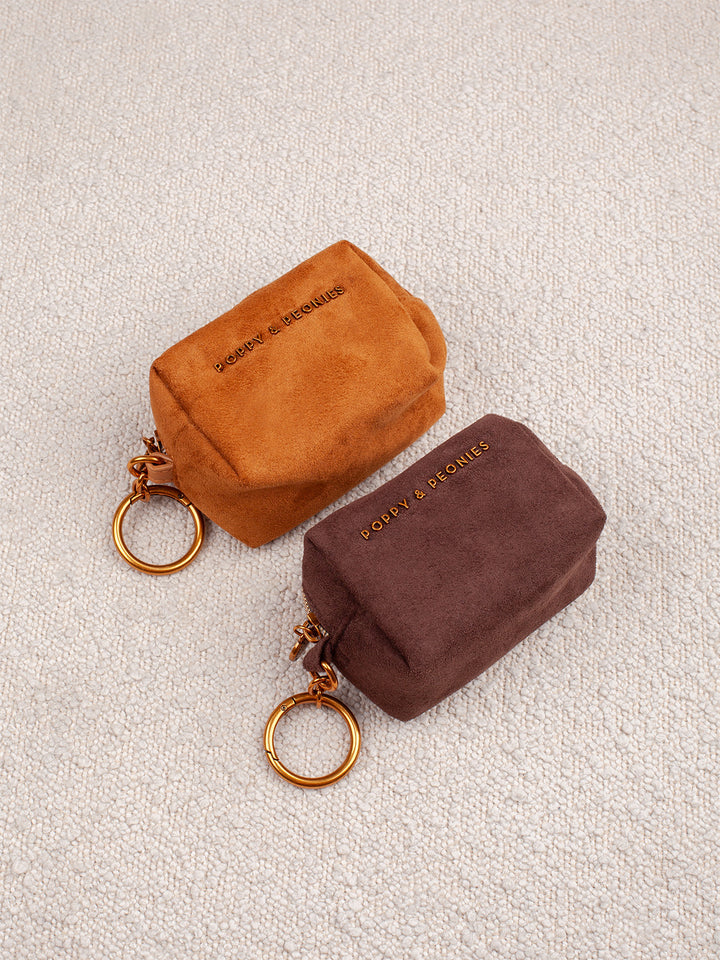 Poppy & Peonies Tag Along Charms in Cognac Suede and Espresso Suede displayed together, featuring compact zippered cases with gold-tone key rings.