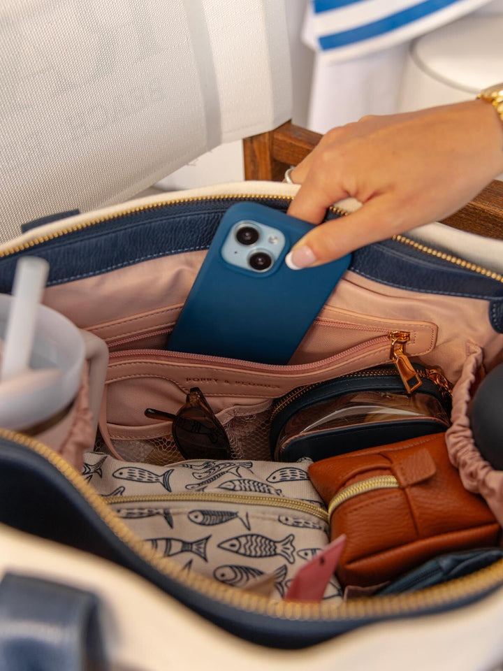 Person placing a blue phone into a suitcase with various items inside.