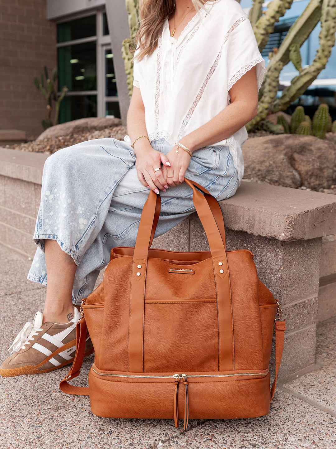 Person sitting on steps holding a brown vegan leather bag with cacti in the background