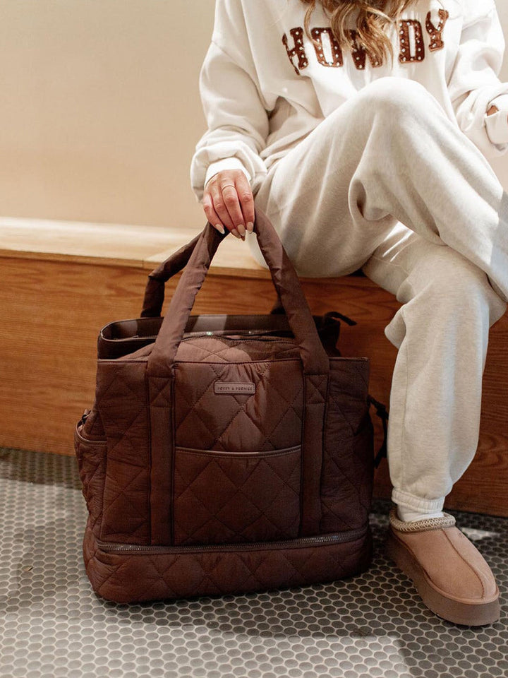 Person holding a brown quilted bag in a casual setting