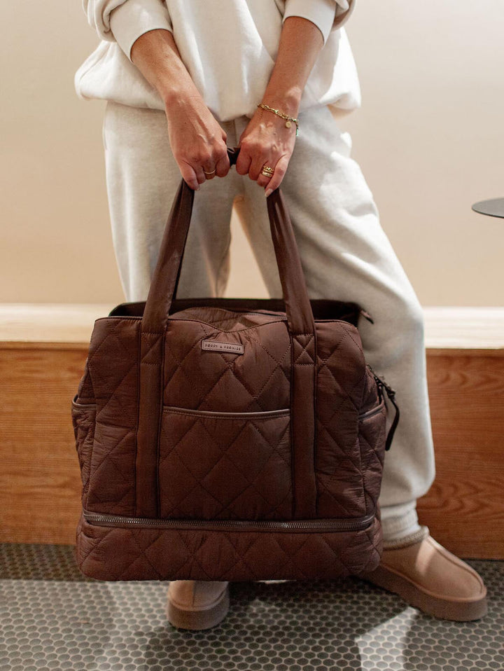Person holding a brown quilted bag indoors