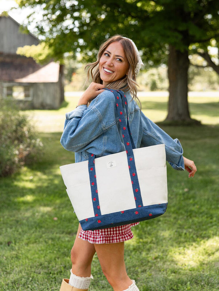 Poppy & Peonies Analog Tote in Strawberry Denim lifestyle view, carried over the shoulder outdoors, featuring a natural canvas body with strawberry-print denim straps and base.