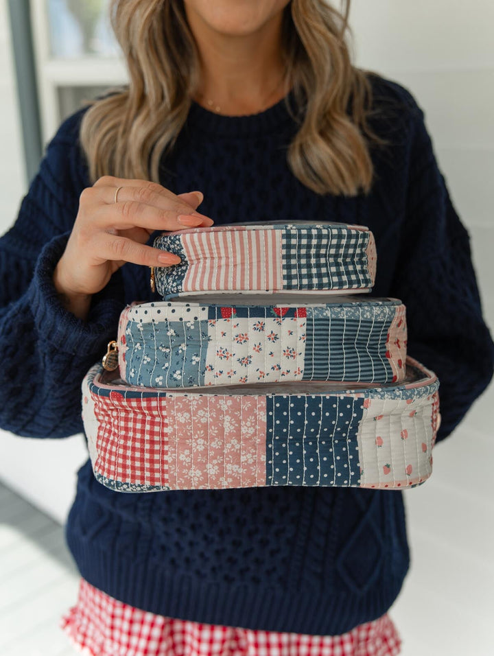 Poppy & Peonies Clearly Organized Set in Strawberry Patchwork lifestyle view, featuring three coordinating quilted organizer cases in small, medium and large sizes stacked and held by a model.