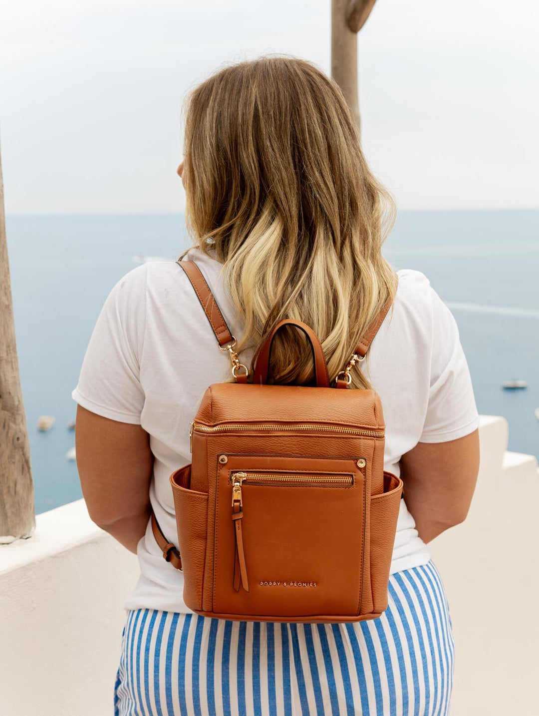 Person wearing a brown vegan leather backpack with a scenic ocean view in the background