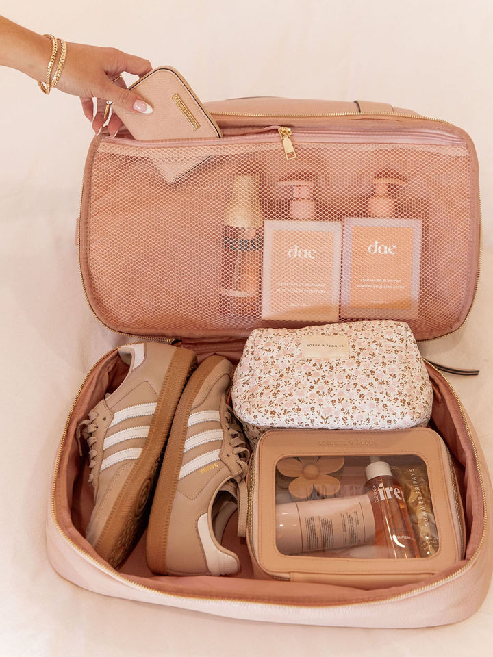 Open pink travel bag with toiletries and sneakers on a light background