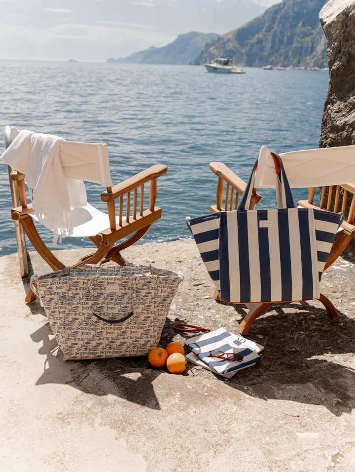 Two wooden chairs with patterned tote bags by a scenic waterfront.