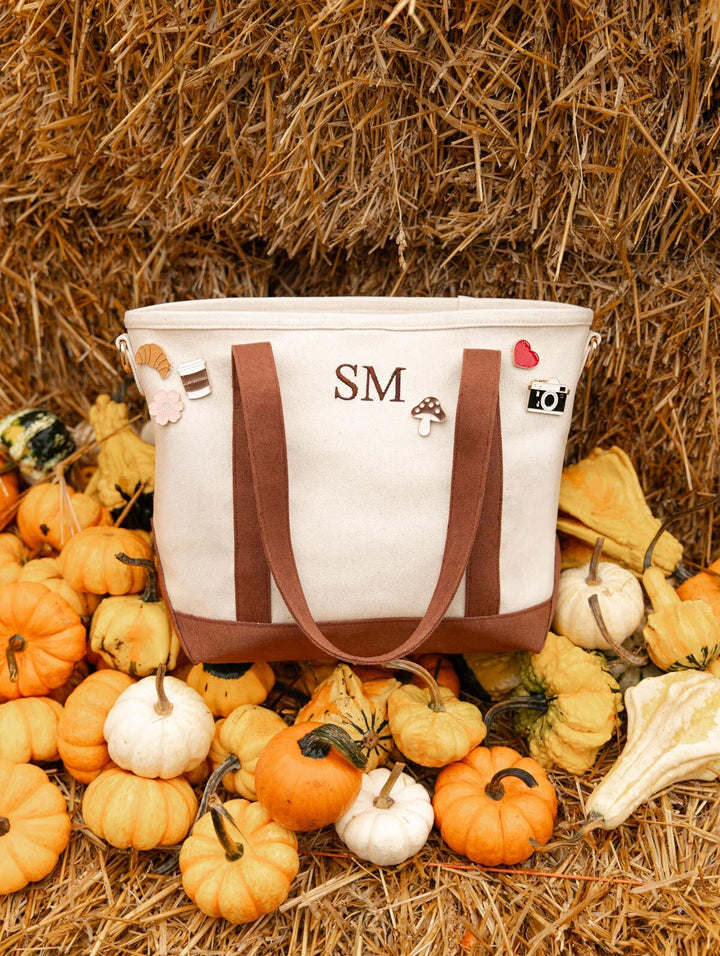 Poppy & Peonies The Small Signature Tote in Chestnut with personalized initials, displayed on a hay bale surrounded by autumn pumpkins and gourds.