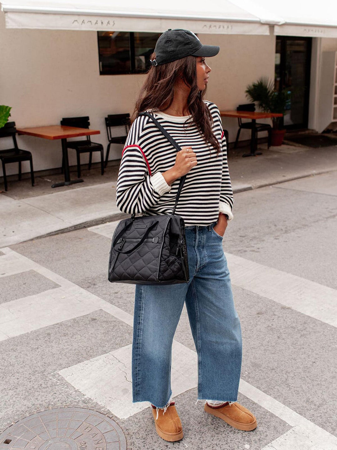 Woman in a striped shirt and jeans holding a black lunch bag on a city street.