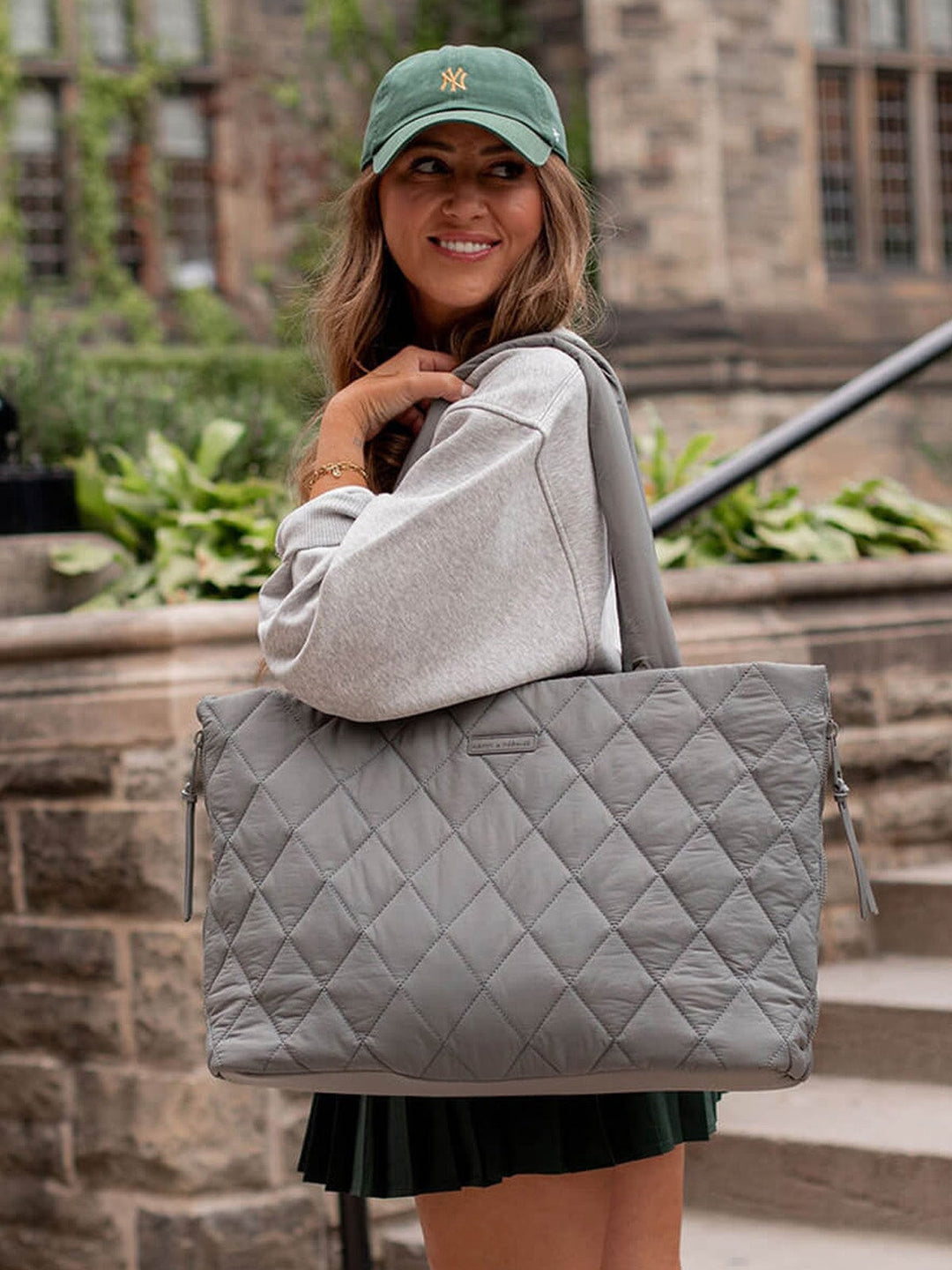 Woman holding a grey quilted tote bag outdoors.