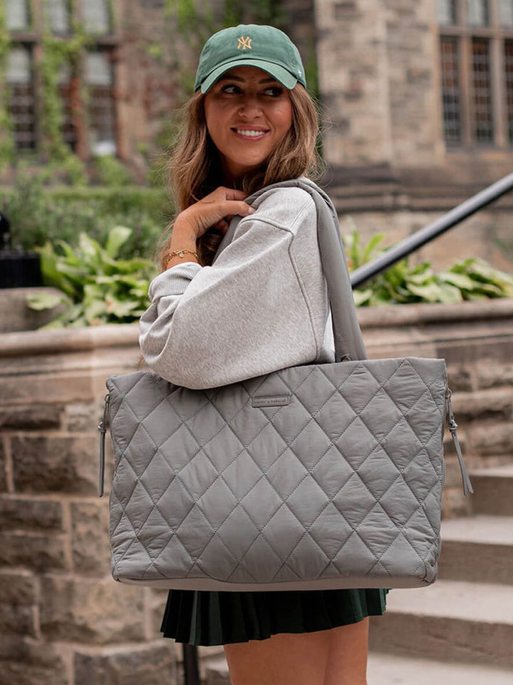 Woman holding a grey quilted tote bag outdoors.