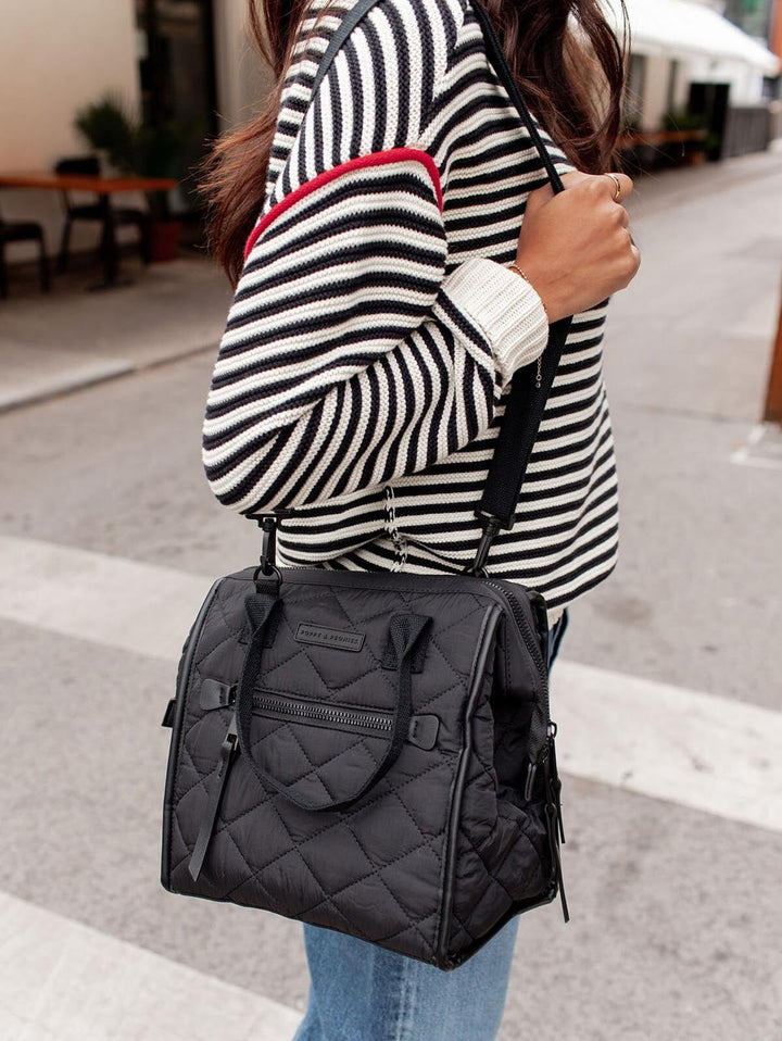 Person wearing a black quilted lunch bag on a city street