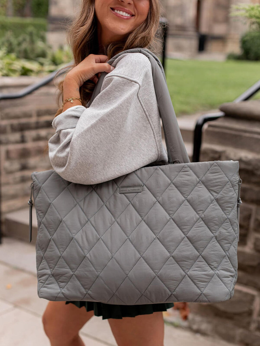 Person holding a quilted grey tote bag outdoors