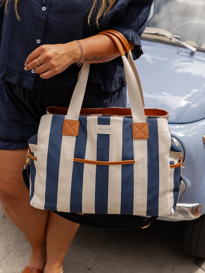 Person holding a blue and white striped bag with brown accents, standing next to a vintage car.