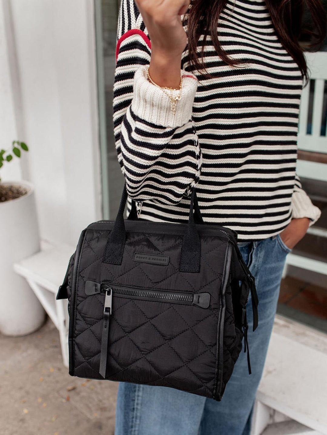 Person holding a black quilted lunch bag with a striped shirt and jeans.
