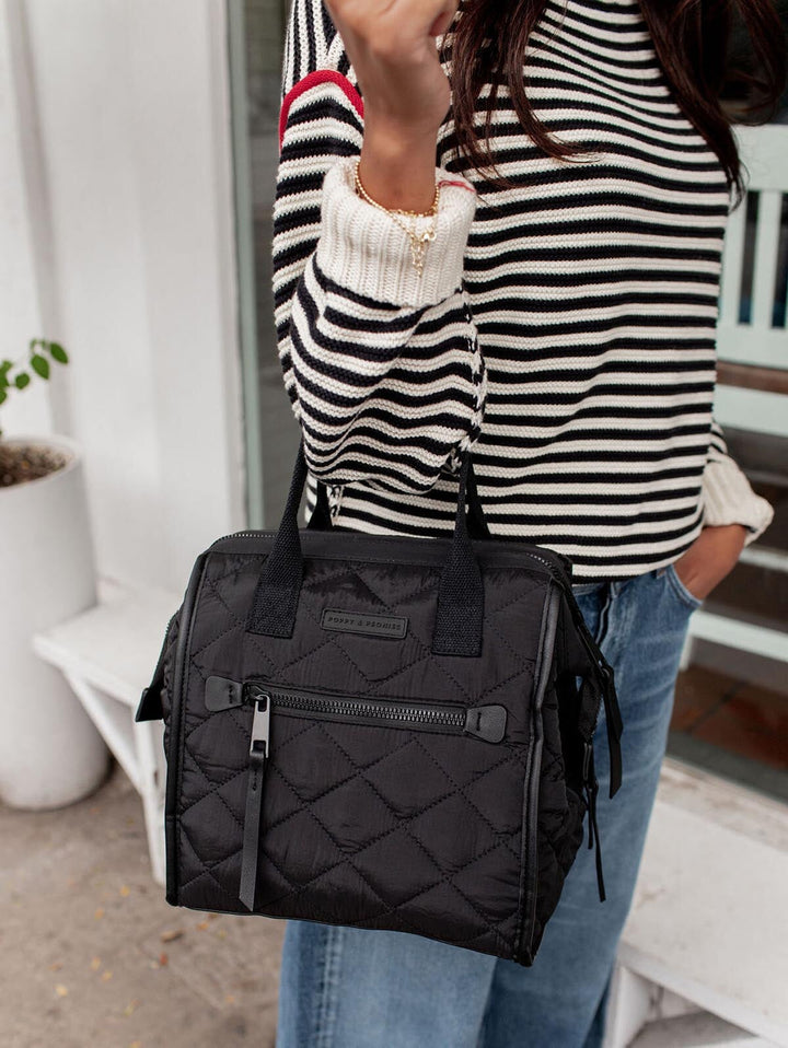 Person holding a black quilted lunch bag with a striped shirt and jeans.