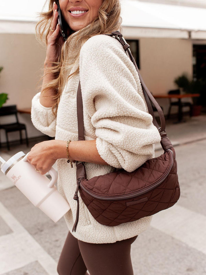 Woman holding a brown quilted handbag and a white water bottle in an outdoor setting.