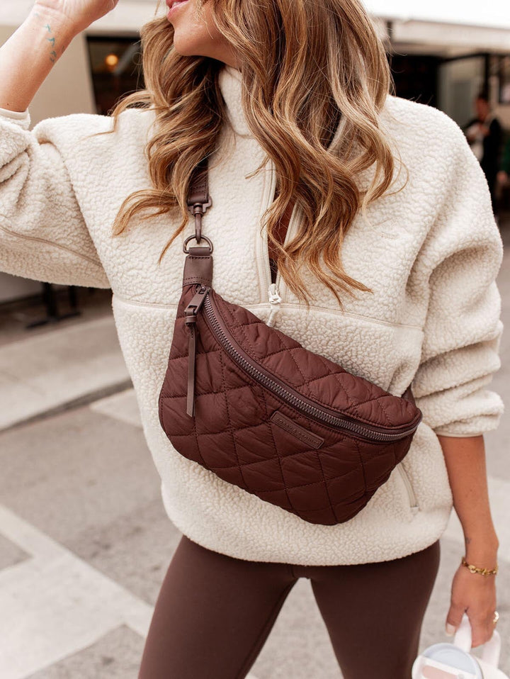 Person wearing a white fleece jacket with a brown quilted bag on a blurred street background