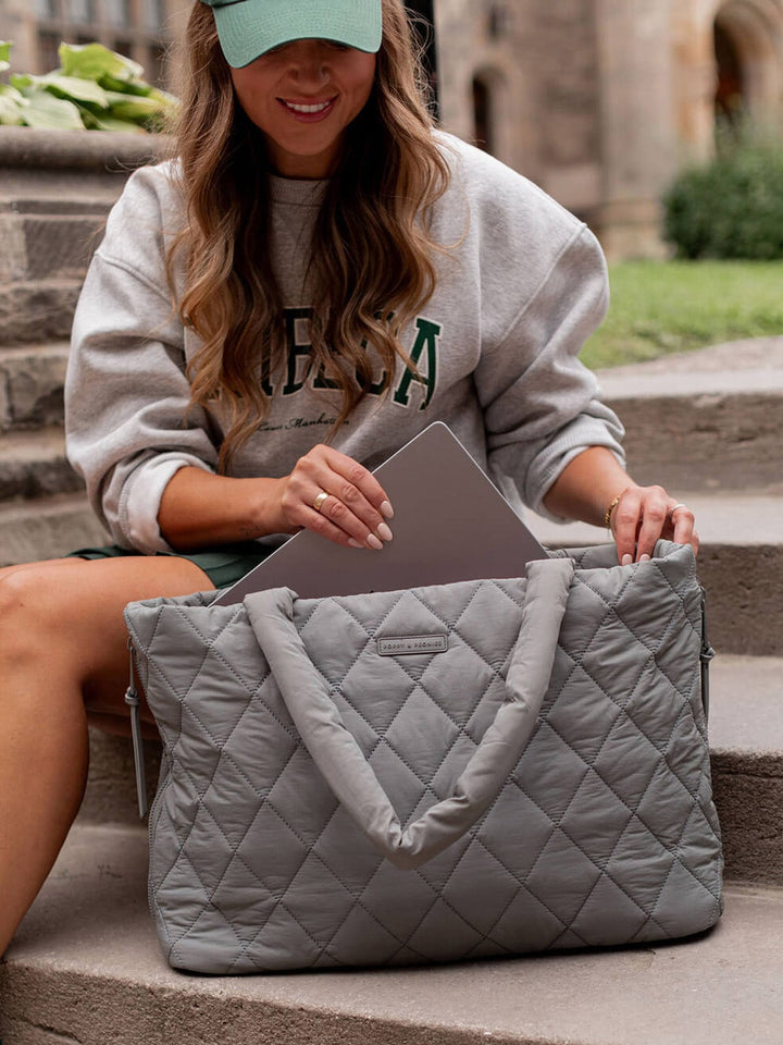 Person sitting on steps with a gray quilted bag and laptop