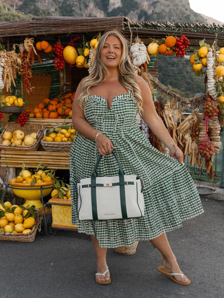 Woman in a green checkered dress holding a white and green bag in front of a fruit stand.