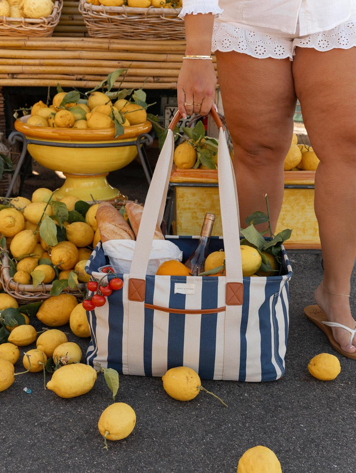Person holding a striped bag filled with lemons and other items in a market setting.
