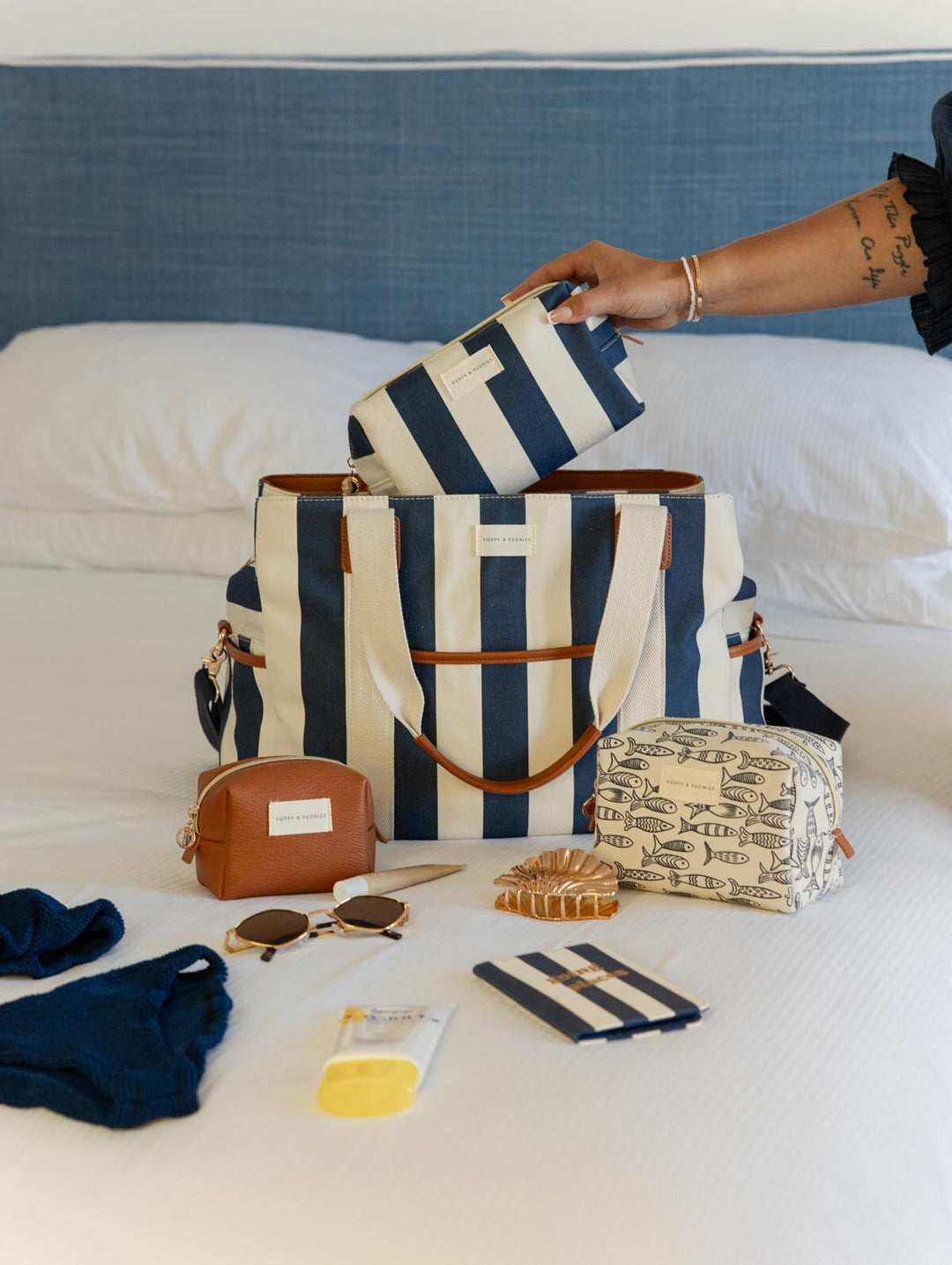 Person organizing striped bags and travel items on a bed