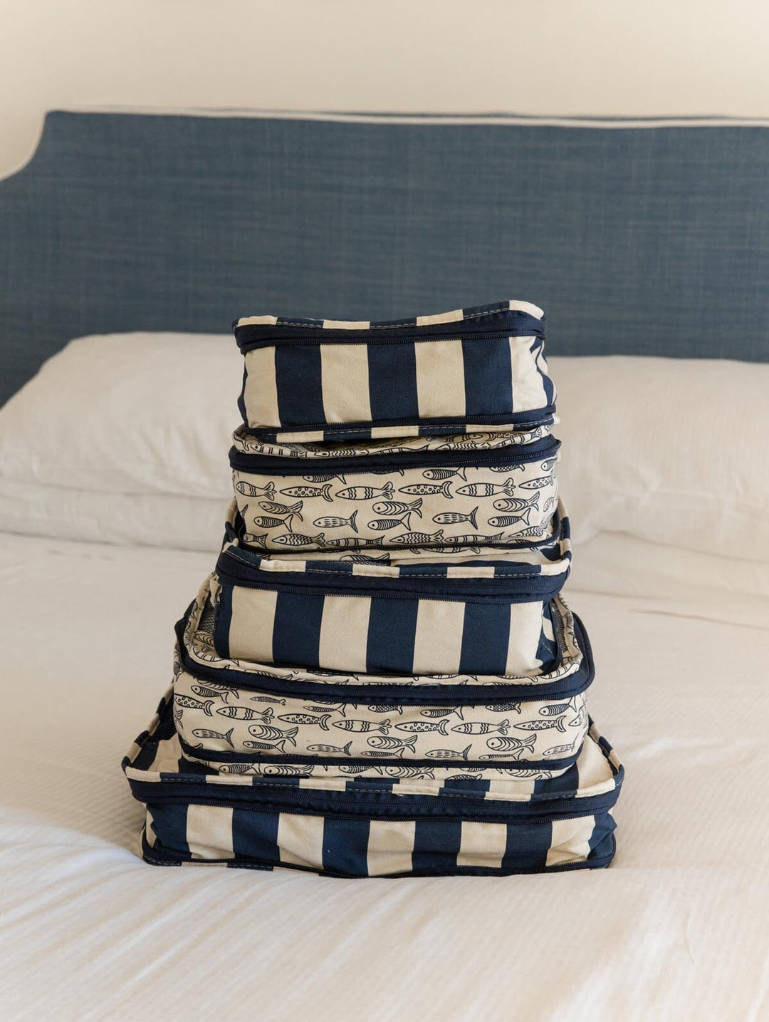 Stack of navy and white striped and patterned fabric baskets on a bed.
