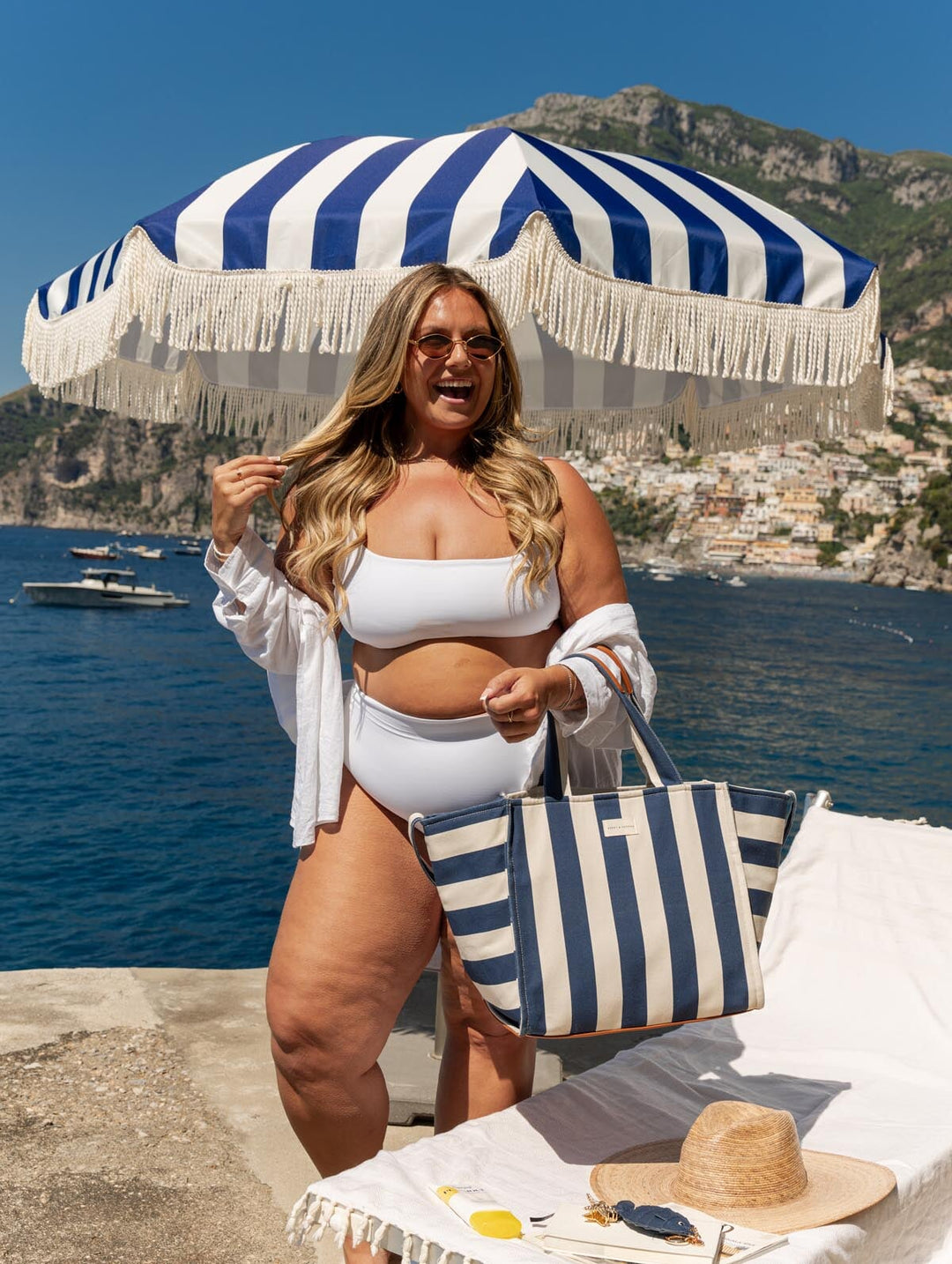 Woman wearing a white bikini and blue and white tote bag with a scenic background