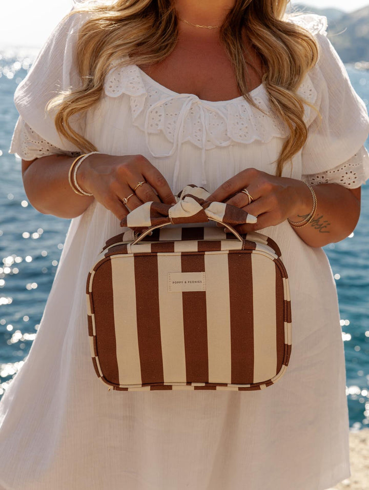 Woman holding a brown and cream striped cosmetic case by the ocean
