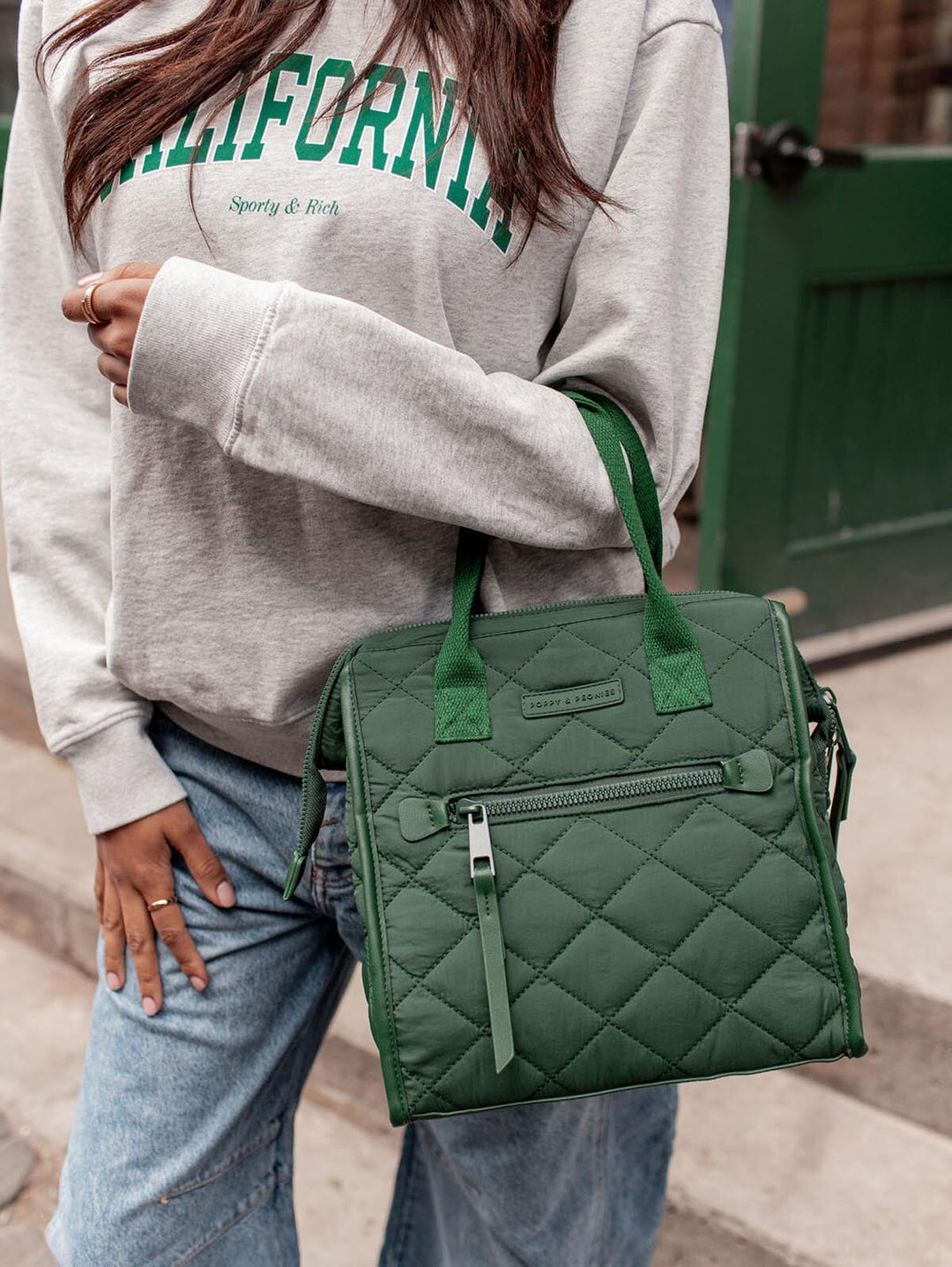 Person wearing a grey sweatshirt with 'California' text, holding a green quilted lunch bag