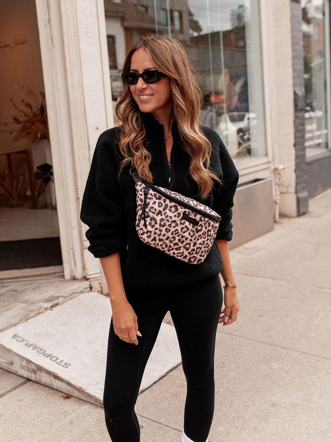 Woman wearing a black outfit with a leopard print crossbody bag on a sidewalk.