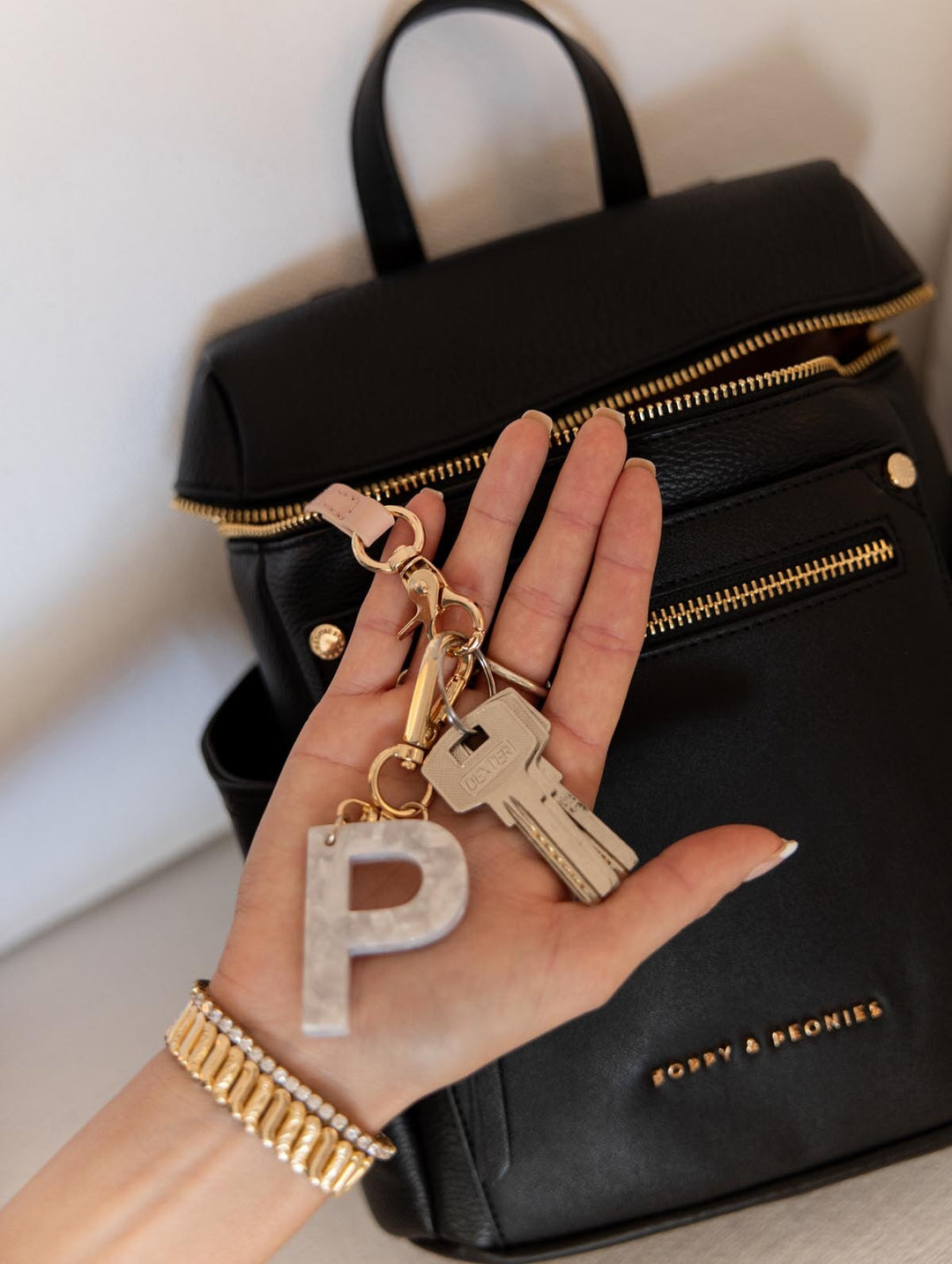 Hand holding a keychain with a letter 'P' in front of a black backpack.